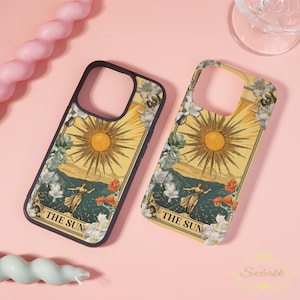 Può includere: Due custodie per telefono con un design di carte dei tarocchi. Le custodie presentano uno sfondo giallo con un'illustrazione del sole, una donna e la scritta "THE SUN". Dettagli floreali e montuosi incorniciano il design. Le custodie hanno un bordo nero.