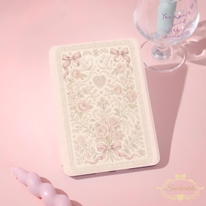 Könnte beinhalten: Eine hellrosa Handyhülle mit einem Blumendesign mit Rosen, Schleifen und Tauben. Die Hülle hat einen dekorativen Rand und ein herzförmiges Design. Eine rosa Kerze und ein Weinglas mit Text sind ebenfalls im Bild.