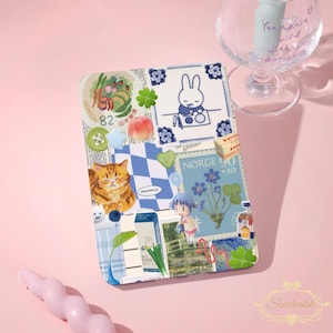Op de afbeelding: Een decoratieve tablethoes met een collage van illustraties en stickers. Het ontwerp bevat een cartoonkat, een konijn, bloemen en postzegels. Het kleurenschema is voornamelijk blauw, wit en perzik, met een vleugje groen. De hoes ligt op een roze ondergrond.