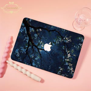 May include: A laptop case with a dark blue floral design featuring a tree branch and small blue and white flowers. The Apple logo is visible. Two spiral candles and a wine glass are also present.
