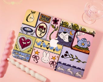 May include: A colorful laptop case with a patchwork design featuring a pear, flowers, a sleeping dog, and a teapot. The case has a variety of pastel colors and whimsical illustrations. The Apple logo is visible in the center.