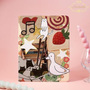 May include: A decorative phone case featuring a collage of whimsical illustrations. The design includes a white cat, a strawberry, musical notes, stars, and a duck. The background has a book theme with a stack of books and a heart.