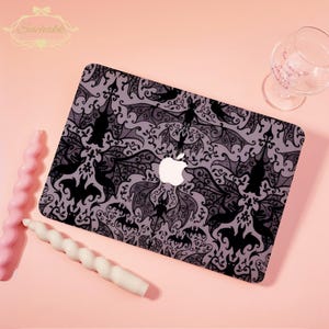 May include: A laptop case featuring a repeating pattern of black bats and ornate swirls on a gray background. The Apple logo is visible. Two spiral candles and a wine glass are also in the image.