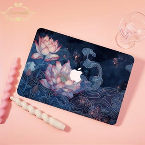 May include: A laptop case with a floral design, showcasing a lotus flower in pink and white against a dark blue backdrop with water patterns. The Apple logo is visible. The case has a glossy finish.