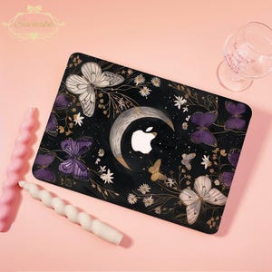 May include: Black laptop skin with a crescent moon, butterflies, and floral details. The design features white, gold, and purple butterflies, and a white Apple logo. The background is black with gold floral accents.