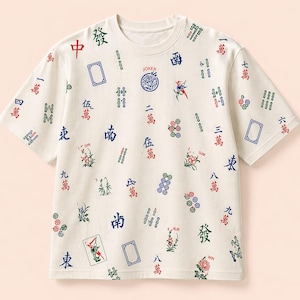 May include: Cream-colored t-shirt with a round neck, featuring a pattern of Mahjong tiles and Chinese characters in red, blue, and green. The word "JOKER" is printed on the shirt. The shirt has short sleeves.