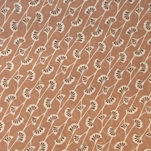 K&ouml;nnte beinhalten: Ein Stoff mit einem sich wiederholenden Muster aus wei&szlig;en, f&auml;cherf&ouml;rmigen Ginkgobl&auml;ttern, die in diagonalen Linien auf einem einfarbigen, terrakottafarbenen Hintergrund angeordnet sind. Das Design erzeugt eine konsistente, strukturierte Textur.