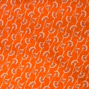 K&ouml;nnte beinhalten: Ein leuchtend orangefarbener Stoff mit einem sich wiederholenden Muster aus wei&szlig;en, diagonalen Linien. Jede Linie ist mit kleinen, f&auml;cherf&ouml;rmigen Blattmotiven verziert, die in einer konsistenten, rhythmischen Abfolge &uuml;ber die gesamte Textiloberfl&auml;che angeordnet sind.
