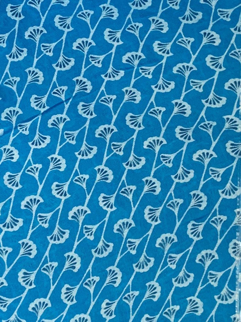 K&ouml;nnte beinhalten: Ein leuchtend blauer Stoff mit einem sich wiederholenden Muster aus wei&szlig;en, stilisierten Ginkgo-Blattmotiven, die in diagonalen Linien angeordnet sind. Das Design besteht aus zarten, d&uuml;nnen Stielen mit f&auml;cherf&ouml;rmigen Bl&auml;ttern und einer Textur.