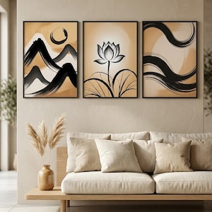 Può includere: Set di tre stampe artistiche astratte incorniciate. Ogni stampa presenta un design nero e beige. Una raffigura montagne e un sole, un'altra un fiore di loto e la terza, pennellate fluide. Sono esposte sopra un divano beige.