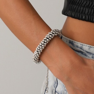 Può includere: Bracciale con perline d'argento. Il bracciale presenta una serie di piccole perline rotonde disposte in file. Una delicata catena si estende dal bracciale per la regolazione. Il bracciale è indossato al polso.