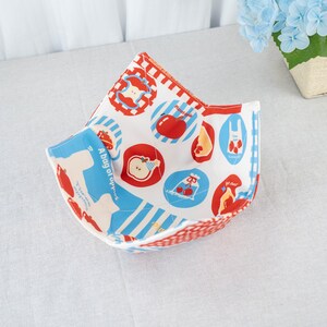 Puede incluir: Un cuenco de tela con exterior de cuadros rojos y blancos e interior blanco estampado con manzanas rojas, rayas azules y el texto "A bag of apples". El cuenco está abierto, mostrando el diseño temático de manzanas.