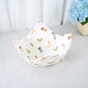 Op de afbeelding: Een witte stoffen kom met een kleurrijk patroon van teckel honden. De honden dragen verschillende outfits in roze, groen, geel en blauw. De kom heeft een open, stervormige vorm en is klaar voor gebruik.