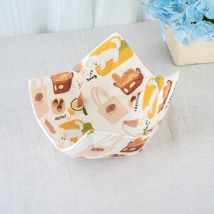 May include: A white fabric bowl with a colorful pattern featuring cartoon dogs, food items, and tote bags. The bowl is open and angled, showcasing the interior design. The pattern includes the word "chestnut".