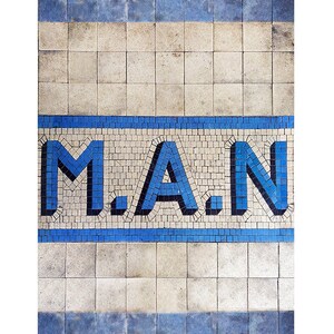 May include: A mosaic tile design featuring the word "M.A.N." in bold blue letters. The letters are set against a background of small, off-white tiles, with blue border lines above and below the text.