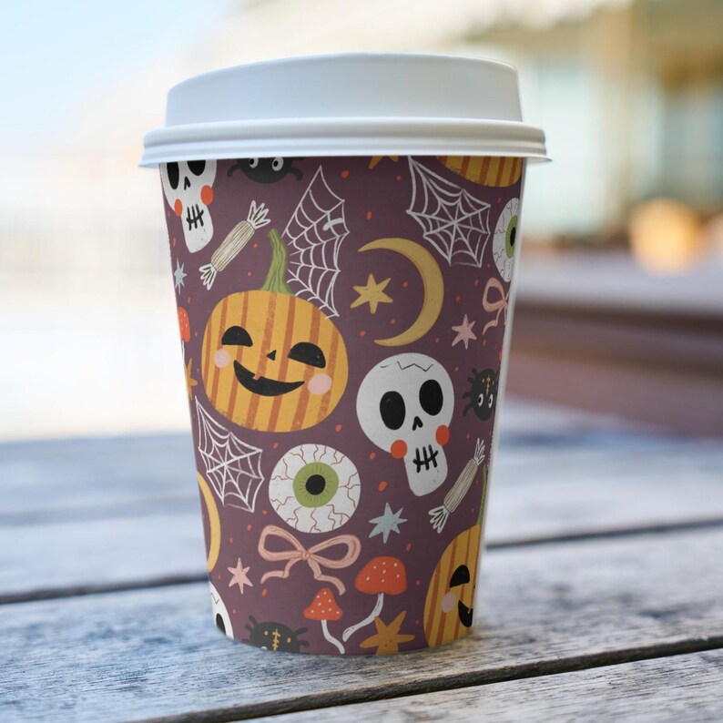 May include: A disposable coffee cup with a white lid, featuring a Halloween-themed pattern. The design includes smiling jack-o'-lanterns, skulls, spiderwebs, and other spooky elements in orange, white, and black on a dark purple background.