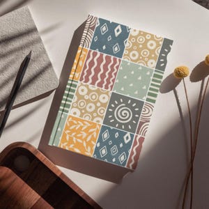 Może przedstawiać: Kolorowy notes z patchworkowym wzorem, kt&oacute;ry zawiera r&oacute;żne kształty geometryczne, spirale i liście. Okładka jest połączeniem ż&oacute;łtego, niebieskiego, zielonego, brązowego i białego.