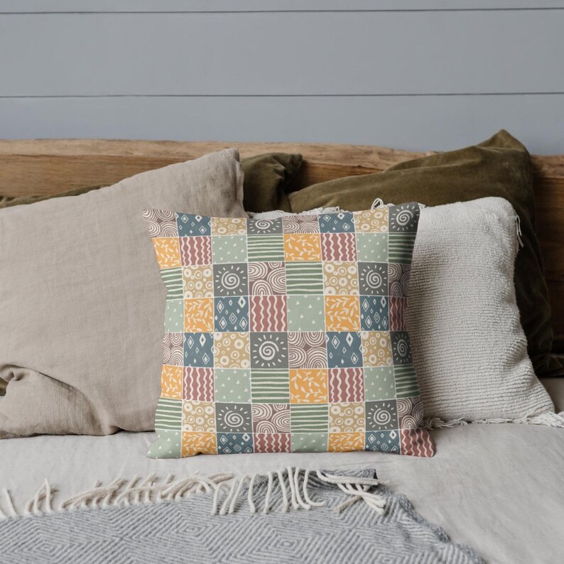 Może przedstawiać: Dekoracyjna poduszka z patchworkowym wzorem, przedstawiającym r&oacute;żne geometryczne kształty i wzory w odcieniach brązu, ż&oacute;łtego, niebieskiego i zielonego.