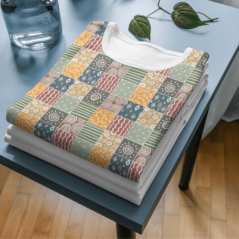 Może przedstawiać: Stos białych koszulek z kolorowym wzorem patchworkowym. Wz&oacute;r zawiera geometryczne kształty, spirale i liście w odcieniach ż&oacute;łtego, pomarańczowego, czerwonego, zielonego i niebieskiego.