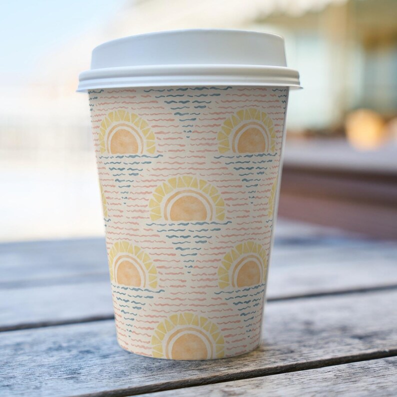 K&ouml;nnte beinhalten: Ein Einweg-Kaffeebecher mit wei&szlig;em Deckel. Der Becher hat ein sich wiederholendes Muster aus gelben Sonnen, die &uuml;ber blauen und rosa Wellenlinien untergehen und eine Strand- und Sommeratmosph&auml;re erzeugen. Der Becher steht auf einer Holzoberfl&auml;che.