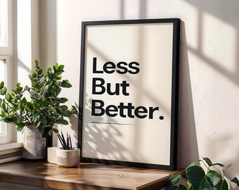 Puede incluir: Una impresión enmarcada con las palabras "Less But Better" en negrita negra. La impresión está en un marco negro y se encuentra sobre una superficie de madera junto a una planta en maceta y un portalápices. El fondo es de color neutro.