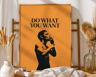 Puede incluir: Póster naranja con el texto "DO WHAT YOU WANT" en negro. El póster presenta una silueta negra de una persona fumando un cigarrillo. El póster está enmarcado en un marco de madera y está apoyado en una escalera de madera.