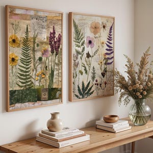 Two framed botanical prints hanging above a wooden console table with books and a vase of dried stems.
