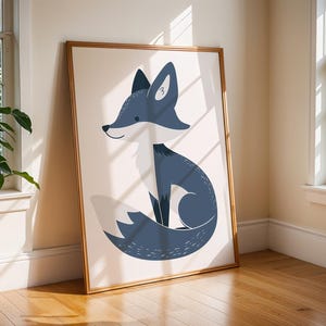 May include: A framed art print featuring a stylized fox illustration. The fox is depicted in shades of blue and white against a cream background. The artwork is encased in a thin, gold-colored frame, leaning against a wall near a window.