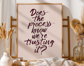 Puede incluir: Impresión enmarcada con el texto "Does the process know we're trusting it?" en escritura borgoña oscuro. La impresión se muestra sobre un fondo rosa claro, con un marco de madera. Parte de una colección de decoración del hogar.