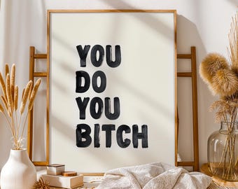 Puede incluir: Impresión artística enmarcada con la frase "YOU DO YOU BITCH" en negrita, con trazos negros. La obra se presenta sobre un fondo crema, enmarcada en madera clara. Un elemento decorativo para el hogar.