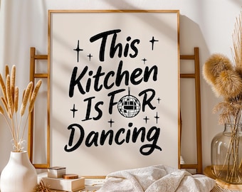 Puede incluir: Impresión enmarcada con el texto "This Kitchen Is For Dancing" en negro. El diseño incluye cruces y una bola de discoteca. El marco es de madera clara y el fondo es beige neutro.