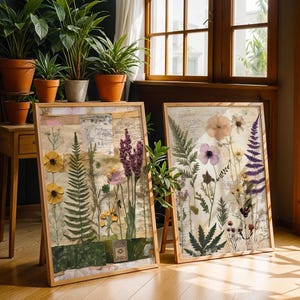 Two framed botanical prints leaning against a wall on a wooden floor near potted plants.