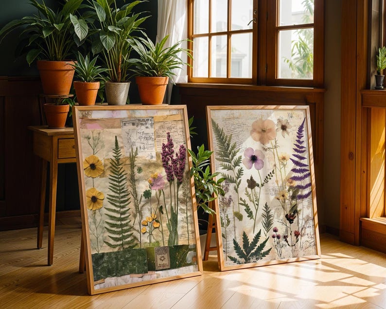 Two framed botanical prints leaning against a wall on a wooden floor near potted plants.