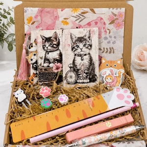May include: A stationery gift box containing two cat-themed notebooks, a 17 cm orange ruler with paw prints, a pink pen, a patterned pen, cat-shaped paper clips, paw-shaped erasers, and cat stickers, all nestled in shredded paper filler.