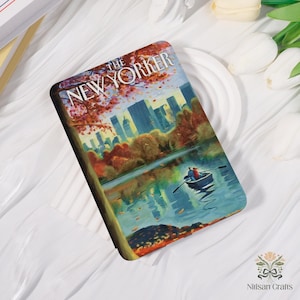 Pode incluir: Artigo decorativo retangular com uma ilustração da capa da revista New Yorker. A obra de arte retrata um casal num barco num lago, com uma paisagem urbana e árvores de outono. O título da revista é visível.