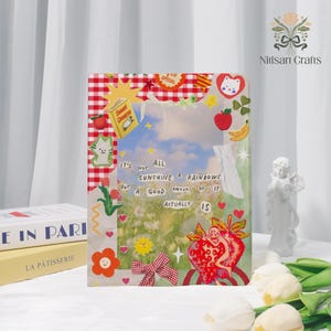 May include: A decorative clear acrylic block with a collage of stickers, including a red gingham border, a yellow star, and a strawberry illustration. The text "It's not all sunshine & rainbows but a good amount of it actually is" is visible.