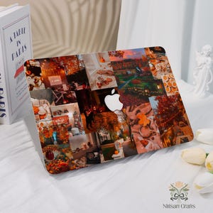 Può includere: Un laptop con un design a collage con scene autunnali nei toni dell'arancione, del marrone e del rosso. Il logo Apple è visibile. Il laptop è su una superficie bianca, con un libro intitolato "A Table in Paris" e una statua bianca sullo sfondo.