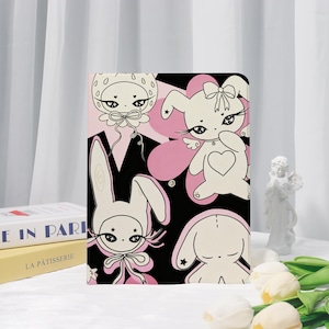 May include: A rectangular tablet case featuring a black background with a repeating pattern of cream-colored cartoon bunnies and strawberry-themed characters. The illustrations include pink accents, heart shapes, stars, and bows with long eyelashes.