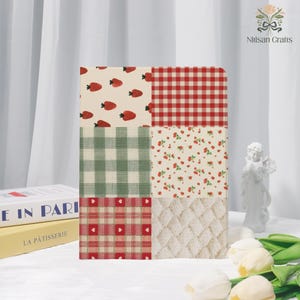 Puede incluir: Un cuaderno decorativo con un diseño de patchwork con fresas, cuadros de vichy y estampados florales en colores rojo, verde y crema. El cuaderno es rectangular y tiene una variedad de texturas y patrones.
