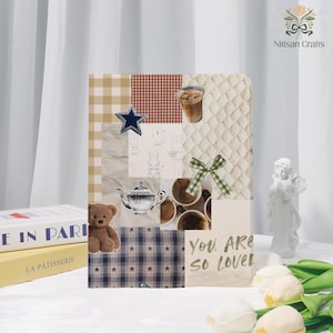 May include: A decorative collage featuring a teddy bear, a teapot, coffee cups, and a blue star. The collage includes the text "You ARE so Loved" and is set against a backdrop of various patterns and textures. A small white statue and tulips are also present.