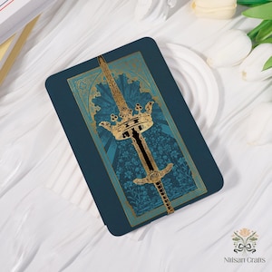 May include: A rectangular teal-colored card featuring a gold and black illustration of a sword and crown. The design has a floral pattern in the background and gold accents. The card is likely a decorative item or a piece of art.