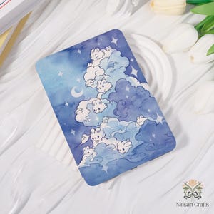 May include: A rectangular phone case featuring a whimsical design of white bunny-shaped clouds floating in a blue watercolor sky with stars and a crescent moon. The case has a glossy finish and a decorative theme.