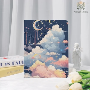 May include: A notebook with a dreamy night sky design. The cover features a crescent moon, stars, and pixelated clouds in shades of blue, pink, and yellow. The notebook is rectangular and appears to be hardcover.