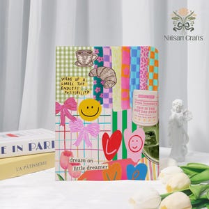 Puede incluir: Un diario colorido con un diseño de collage. La portada presenta un patrón de cuadrícula, ilustraciones de una taza de café, un cruasán, una carita sonriente, lazos, corazones y el texto "WAKE UP & SMELL THE ENDLESS POSSIBILITY" y "dream on little dreamer".