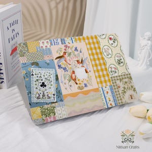 Op de afbeelding: Een decoratieve laptophoes met een patchwork-ontwerp met bloemen-, vogel- en speelkaartmotieven. De hoes heeft een verscheidenheid aan patronen, waaronder ruitjes en bloemenprints. De hoes heeft een pastelkleurenpalet.