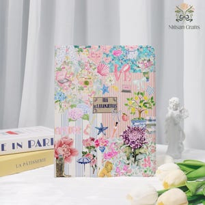 Pode incluir: Um diário decorativo com um design de colagem floral. A capa apresenta uma mistura de flores, estrelas e a palavra "LOVE". O diário tem um padrão de listras verticais com as palavras "AMORE" e "RUA DAS LARANJEIRAS".