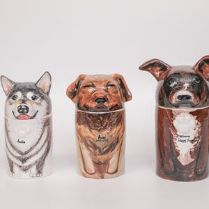 May include: Three ceramic dog-shaped containers. The first is a husky with the name "Andie". The second is a brown dog with the name "Ace". The third is a brown dog with the name "Winnie Happy Forever".