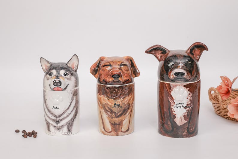 May include: Three ceramic dog-shaped containers. The first is a husky with the name "Andie". The second is a brown dog with the name "Ace". The third is a brown dog with the name "Winnie Happy Forever".