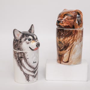 May include: Two ceramic dog-themed containers. One features a husky design with black, white, and gray fur, and the name "Anda". The other has a brown dog design with the name "Ace".