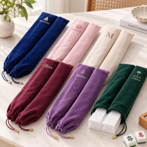 May include: A collection of six velvet drawstring pouches in navy, pink, cream, burgundy, purple, and dark green. Each pouch features custom embroidery including names like Olivia and Emma, or logos like Harbor Lane and Good Games.